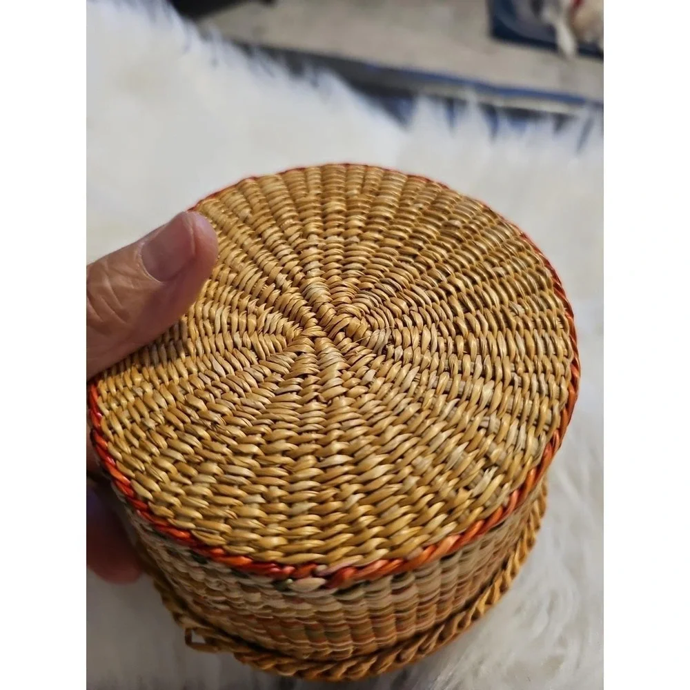The image displays a‎ small, round, hand-woven basket with a lid, typically made
